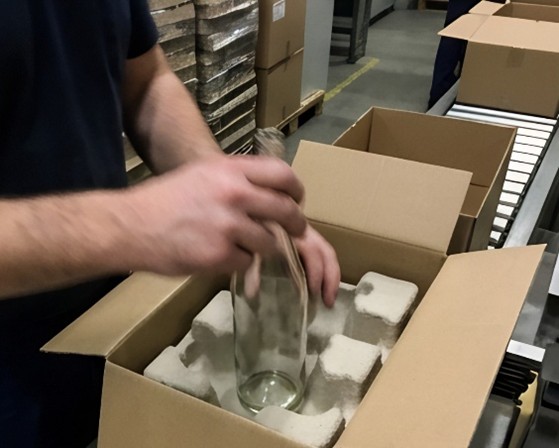 Real-time handling of a glass bottle being placed into a custom molded pulp protective insert inside a shipping box.